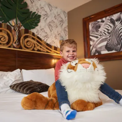 Boy on a bed with a toy tiger in a Zebra room in the Chessington Safari Hotel